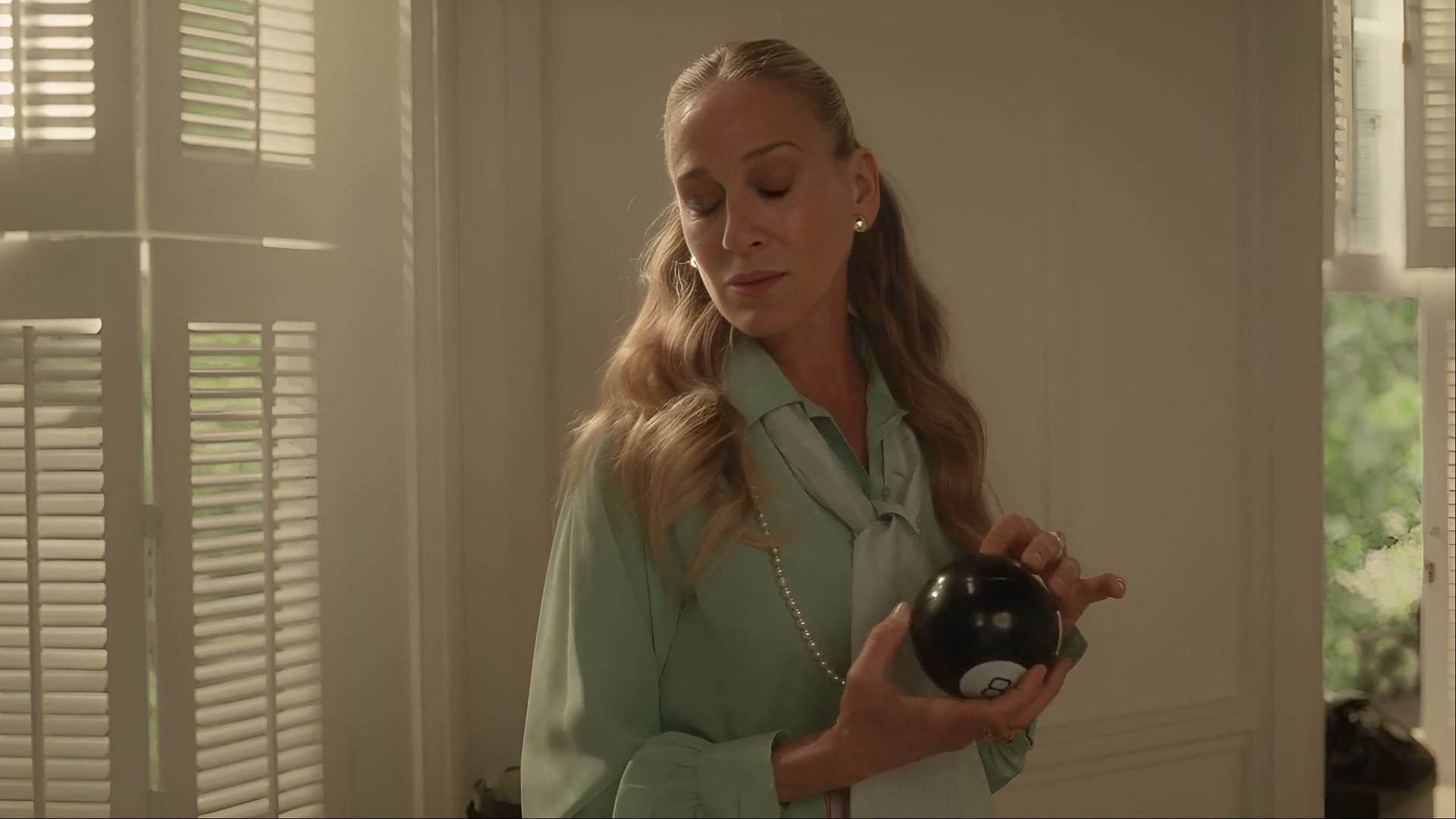 Carrie Bradshaw holds a Magic 8-Ball as she contemplates her next move in And Just Like That season 3. (Image via Now)